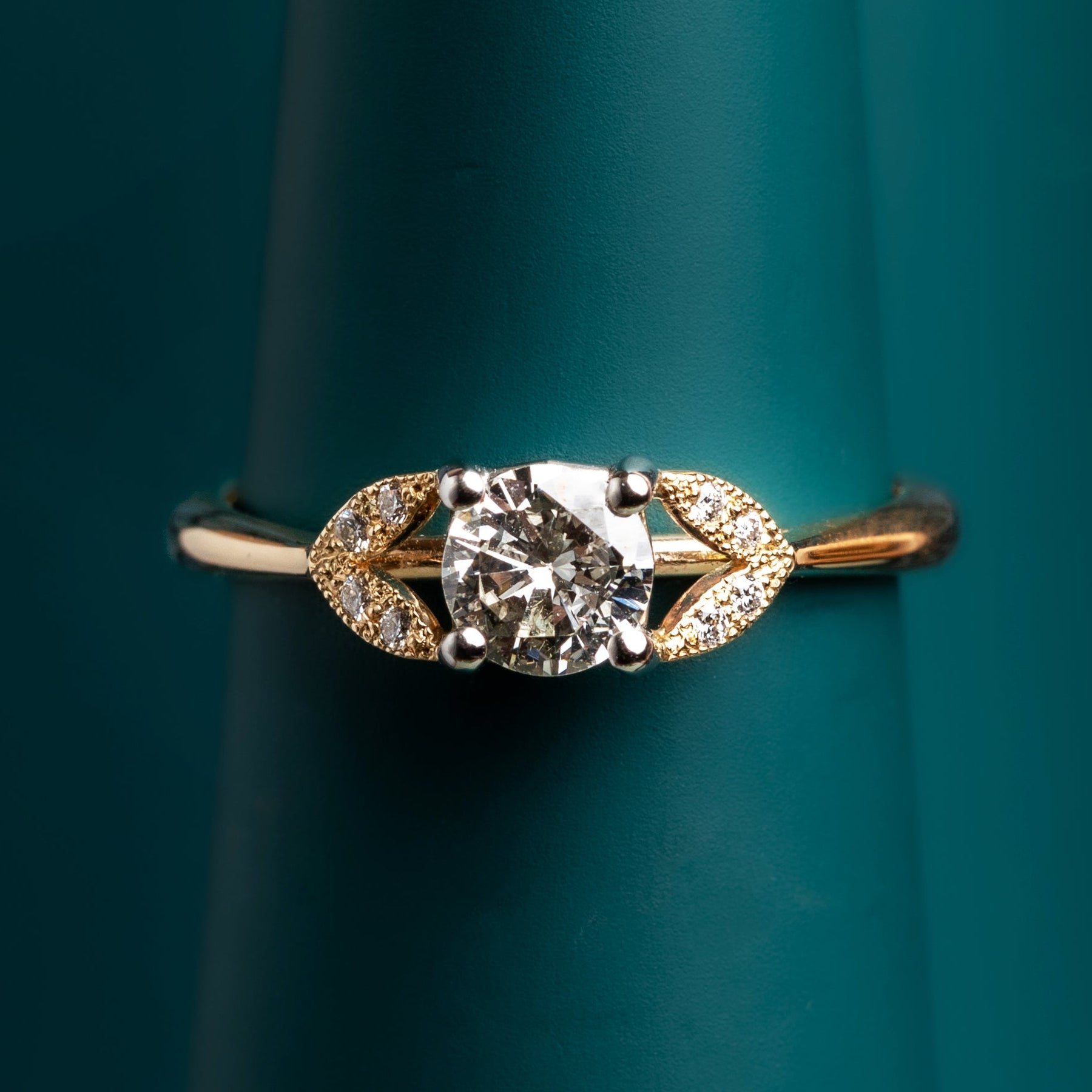 Gold and reclaimed diamond ring with leaf details on a teal background
