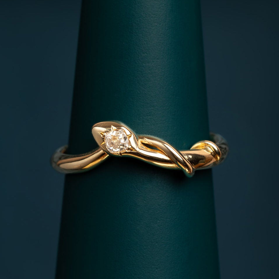 Gold handmade snake ring with a star set diamond on a green stand against a dark background