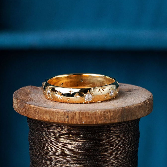 Gold ring with engraved stars and star set diamonds on a wooden spool against a blue background